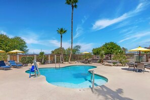 A swimming pool with lounge chairs and umbrellas, surrounded by a fence and palm trees.