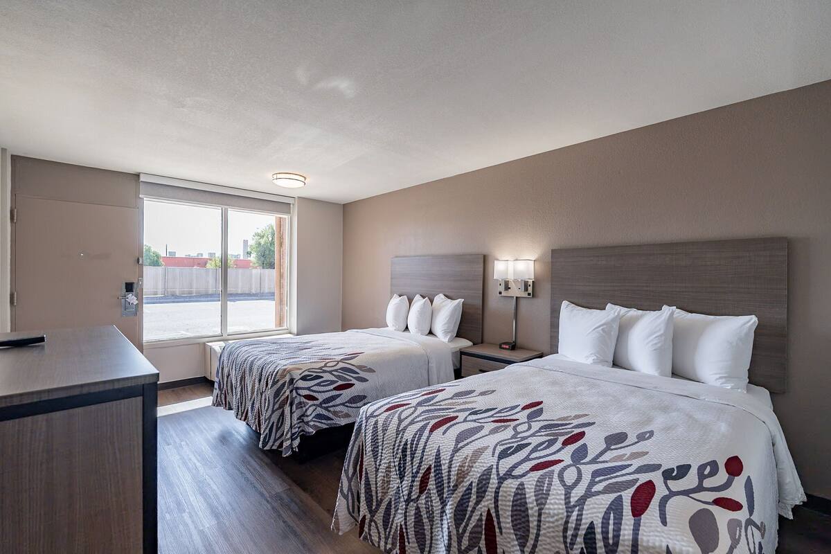 Une chambre d’hôtel avec deux lits, un bureau et une fenêtre donnant sur l’extérieur.
