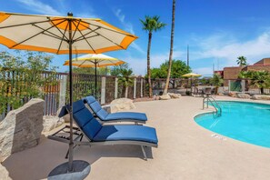 A poolside area with lounge chairs and umbrellas, a clear blue sky, and palm trees.