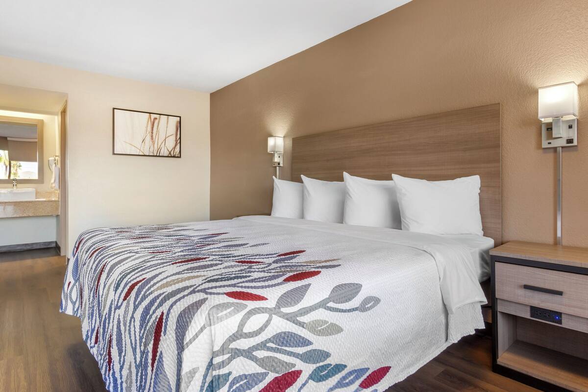 Une chambre d’hôtel avec un grand lit, une table de chevet, une commode, une lampe fixée au mur et un tableau encadré accroché au mur.