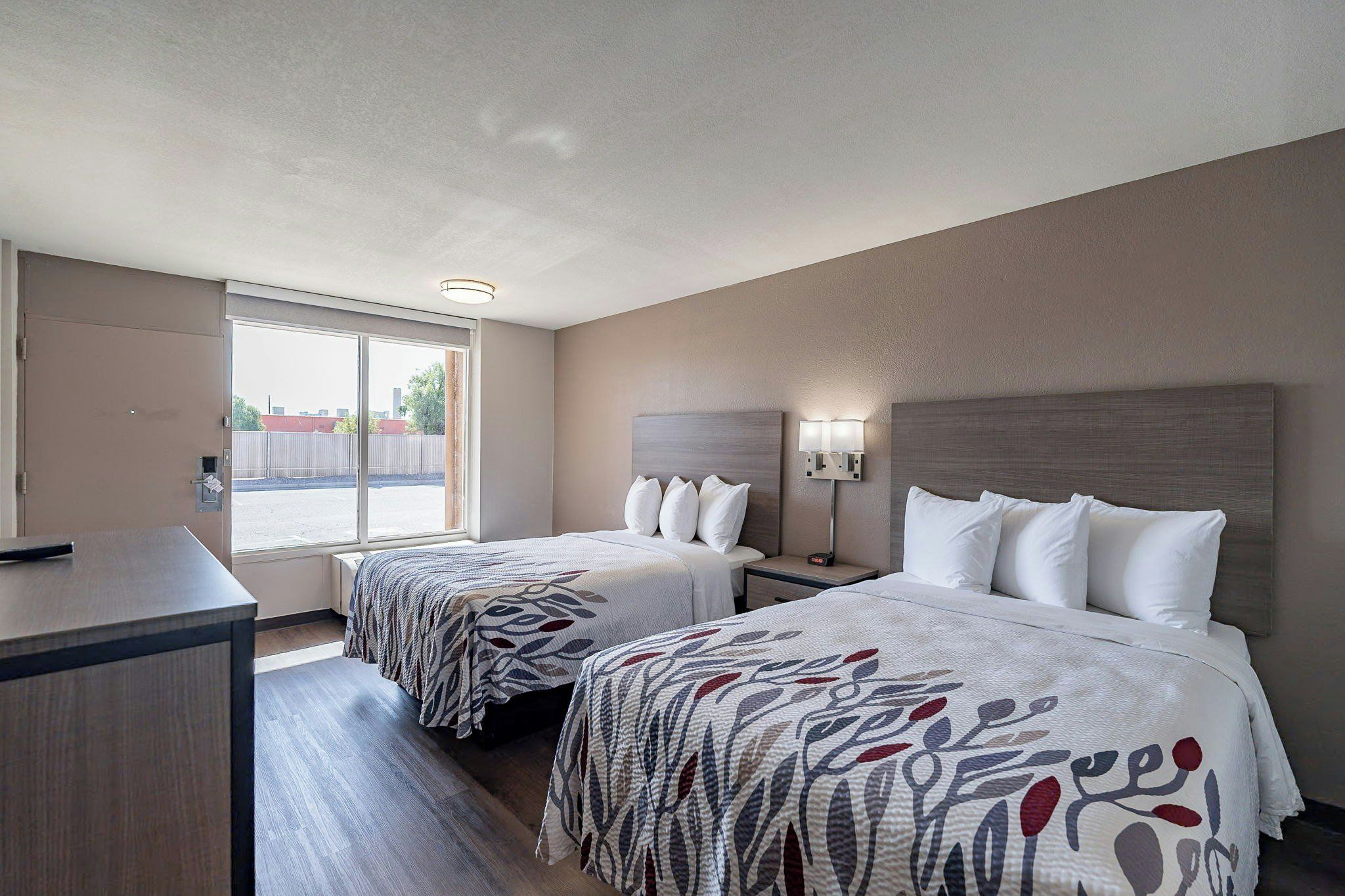 Habitación de hotel con dos camas, un escritorio y una ventana que ofrece vistas al exterior.