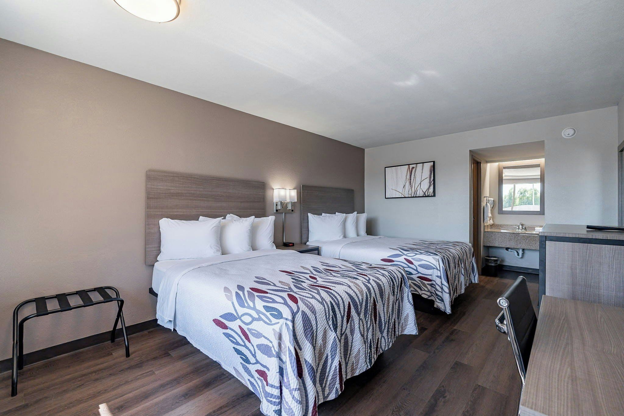Quarto de hotel com duas camas, uma mesa, uma cadeira e um banheiro.