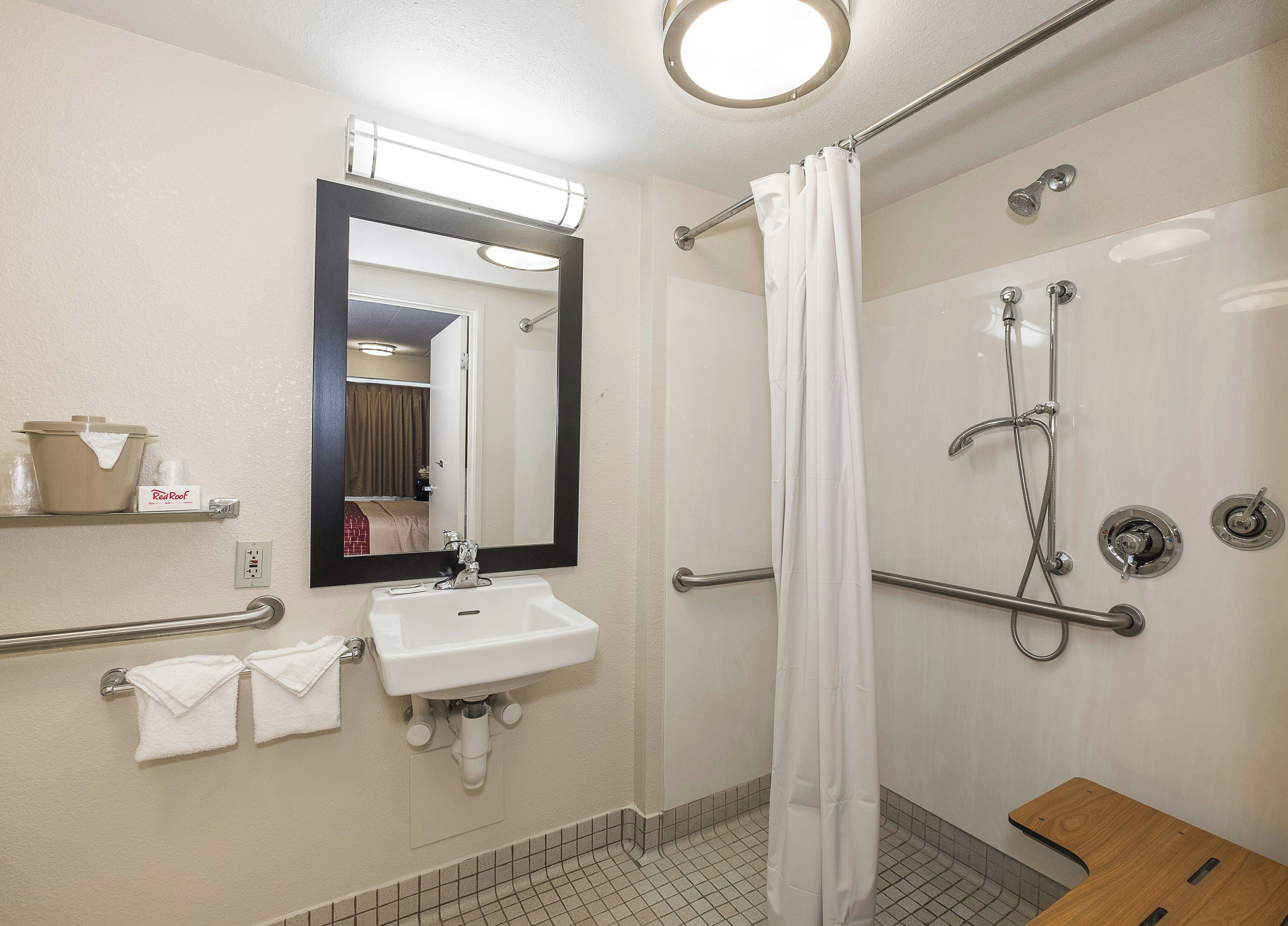 A bathroom with a sink, mirror, shower, and grab bars.