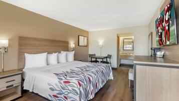 A hotel room with a bed, bedside table, desk, chair, and a large mirror.