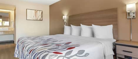 A hotel room with a bed, a bedside table, a nightstand, a lamp, and a painting on the wall.
