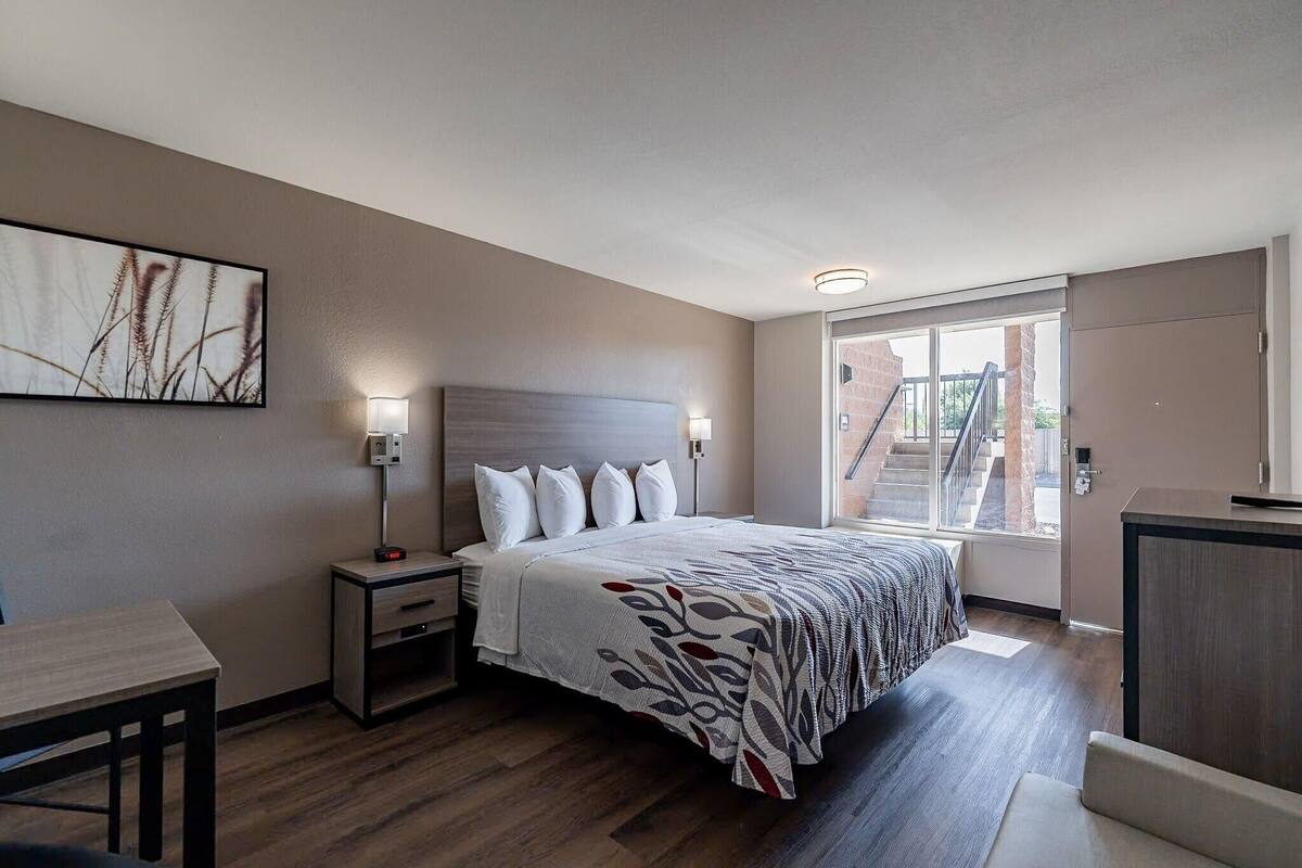 Une chambre d’hôtel moderne, dotée d’un grand lit, de tables de chevet, d’un bureau et d’une fenêtre donnant sur l’extérieur.