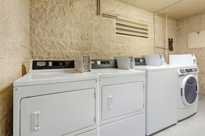 A laundry area with stacked washers and dryers, a control panel, and a vent on the wall.