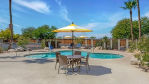 A pool area with lounge chairs and umbrellas, surrounded by palm trees and a fence. - Red Roof Inn Tucson South - Airport (Tucson)