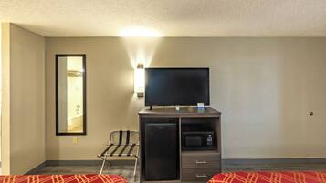 A hotel room with a bed, a desk with a flat-screen TV, a microwave, and a small refrigerator.