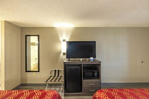 Habitación de hotel con cama, escritorio, televisor de pantalla plana, microondas y refrigerador pequeño.