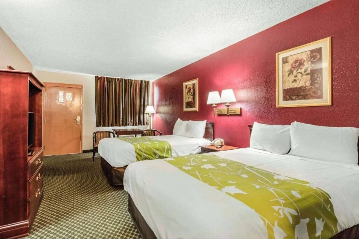 A hotel room with two beds, a wooden wardrobe, a desk with a telephone, and a framed picture on the wall.