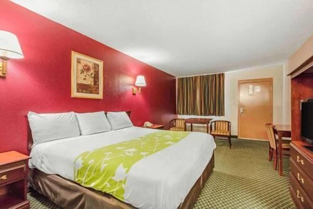 A hotel room with a bed, a desk, a chair, a television, and a door.