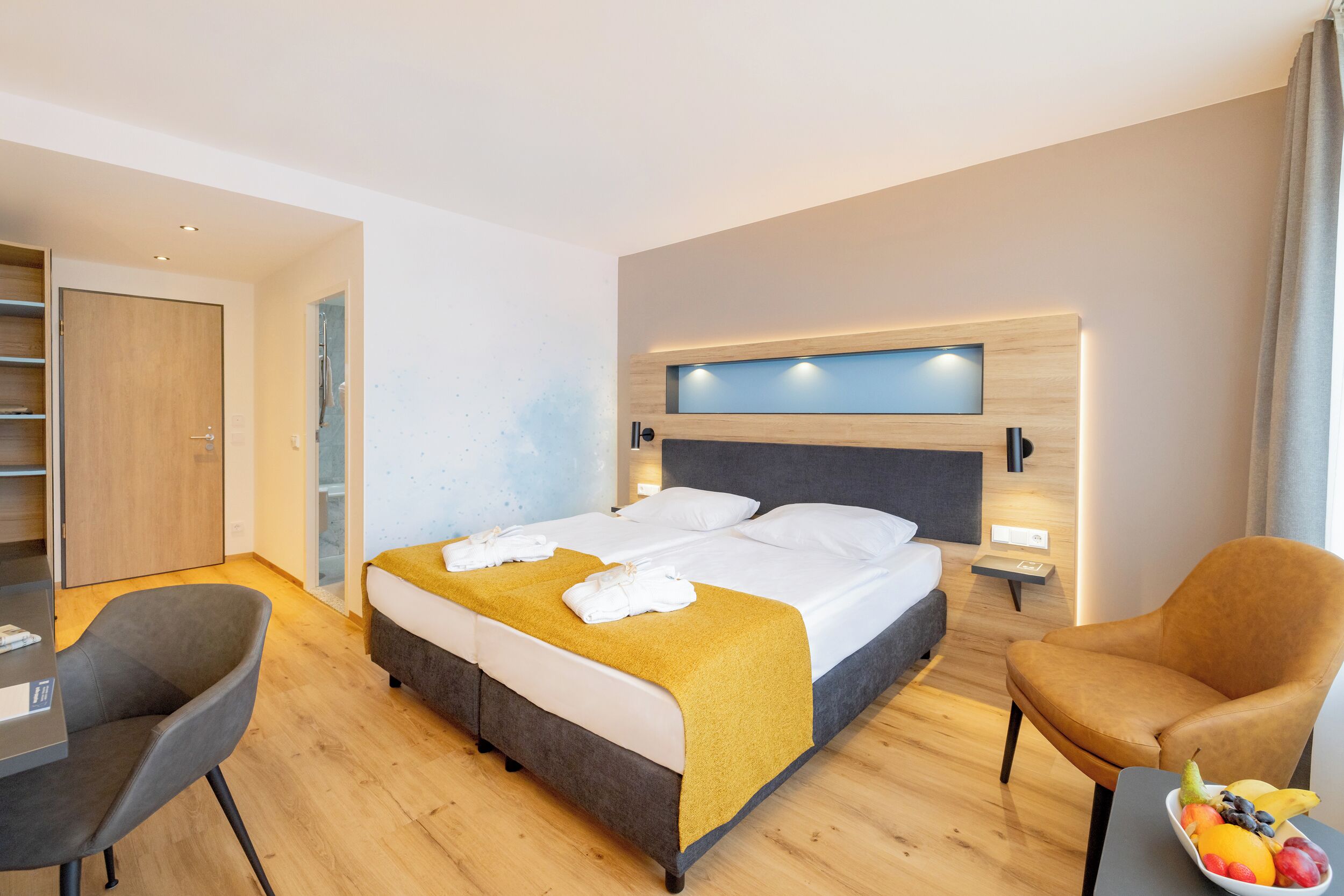 Une chambre d’hôtel avec un lit, deux chaises, un bureau et un panier de fruits.