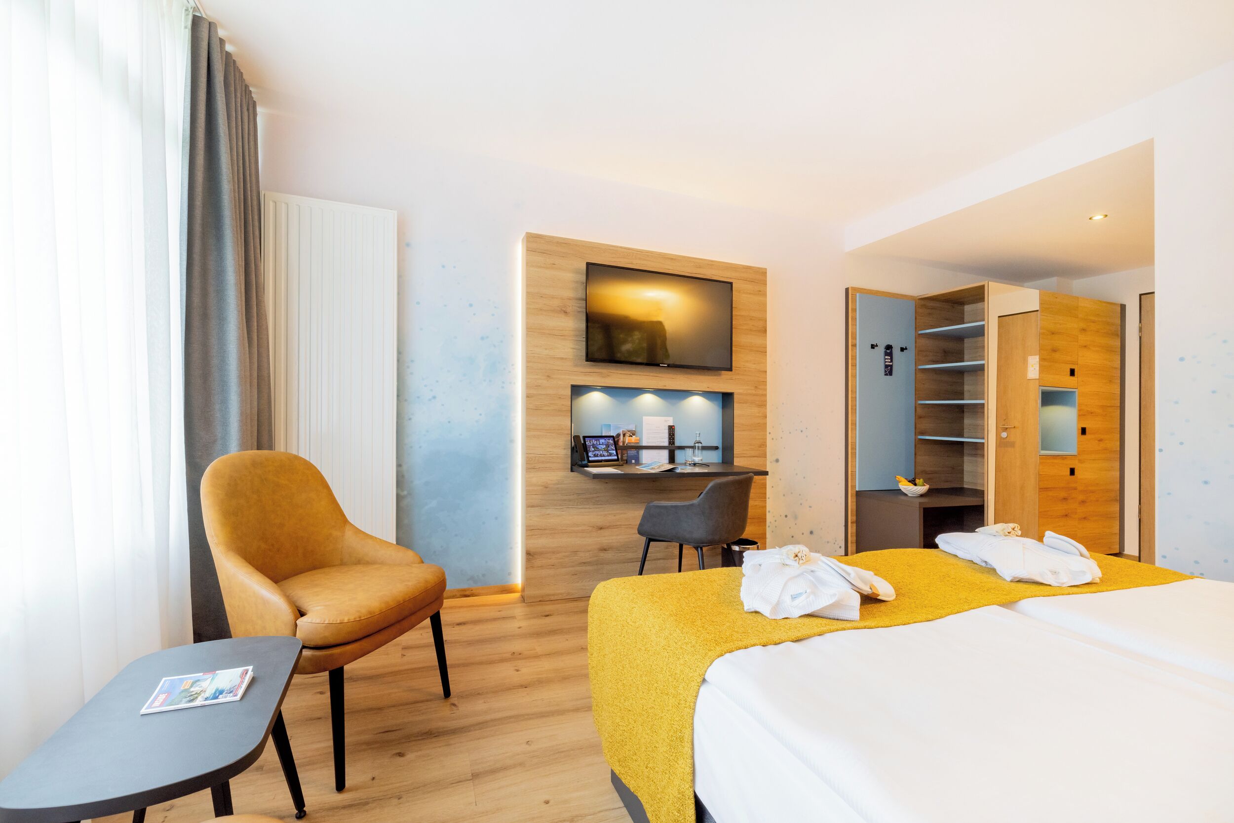 Habitació d'hotel amb un llit, una taula de treball, una cadira i un armari.