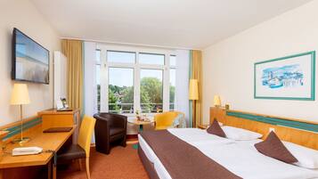 Ein Hotelzimmer mit Bett, Schreibtisch, Stühlen und Blick auf Grün hinter dem Fenster.