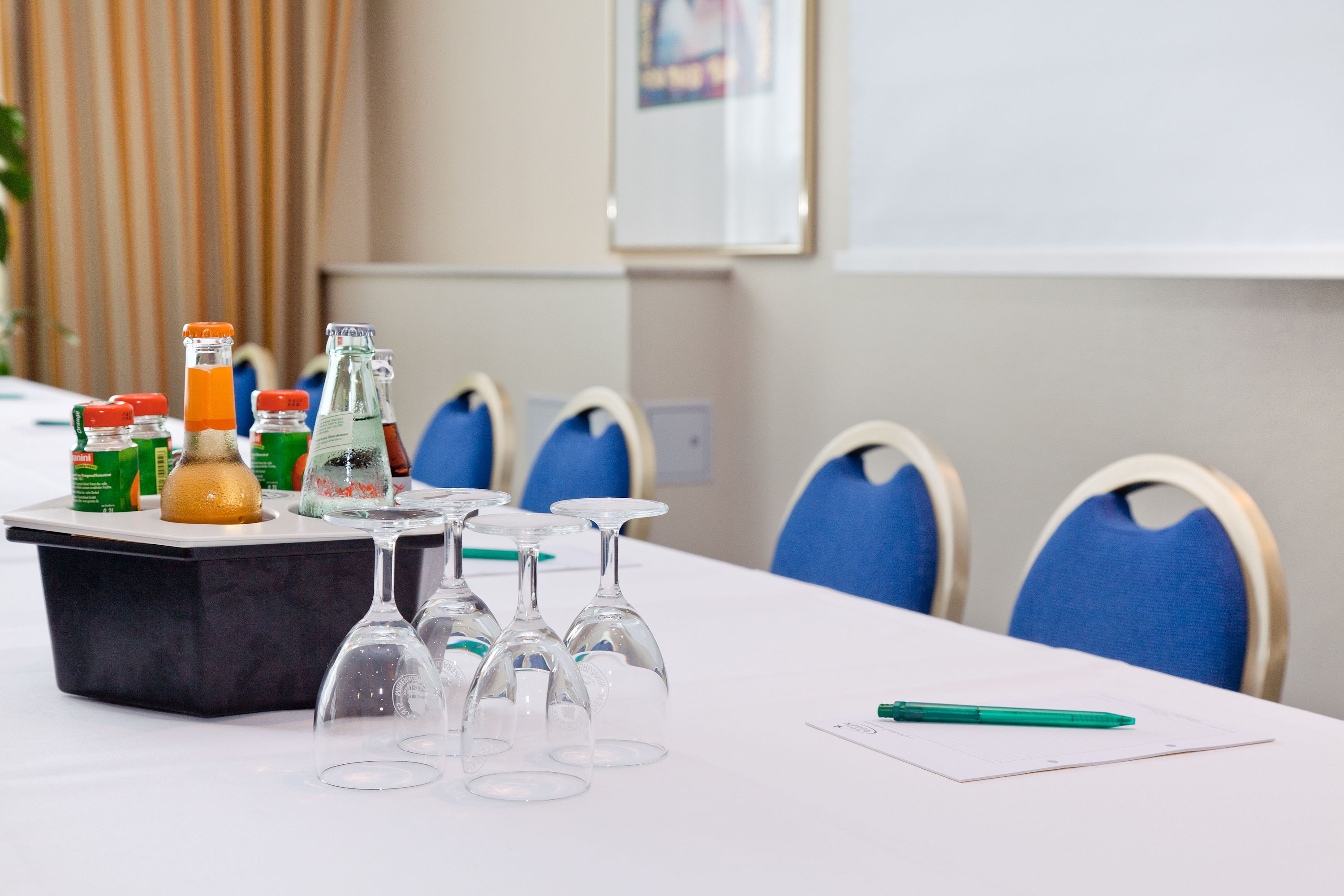 A conference table with wine glasses, bottles, and a pen.