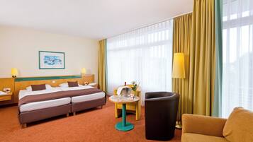 Una habitación de hotel con cama, dos sillones, una mesita y una lámpara.