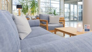 Un espace de détente moderne avec un ensemble de canapés gris, des tables d’appoint en bois et de grandes fenêtres donnant sur l’extérieur.