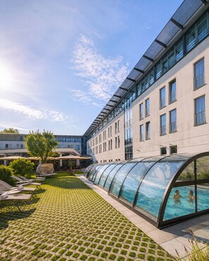 A modern building with a swimming pool, lounge chairs, and a covered walkway.