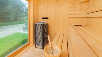 Una sala de sauna con paredes de madera, un banco, un balde y un calentador de sauna.