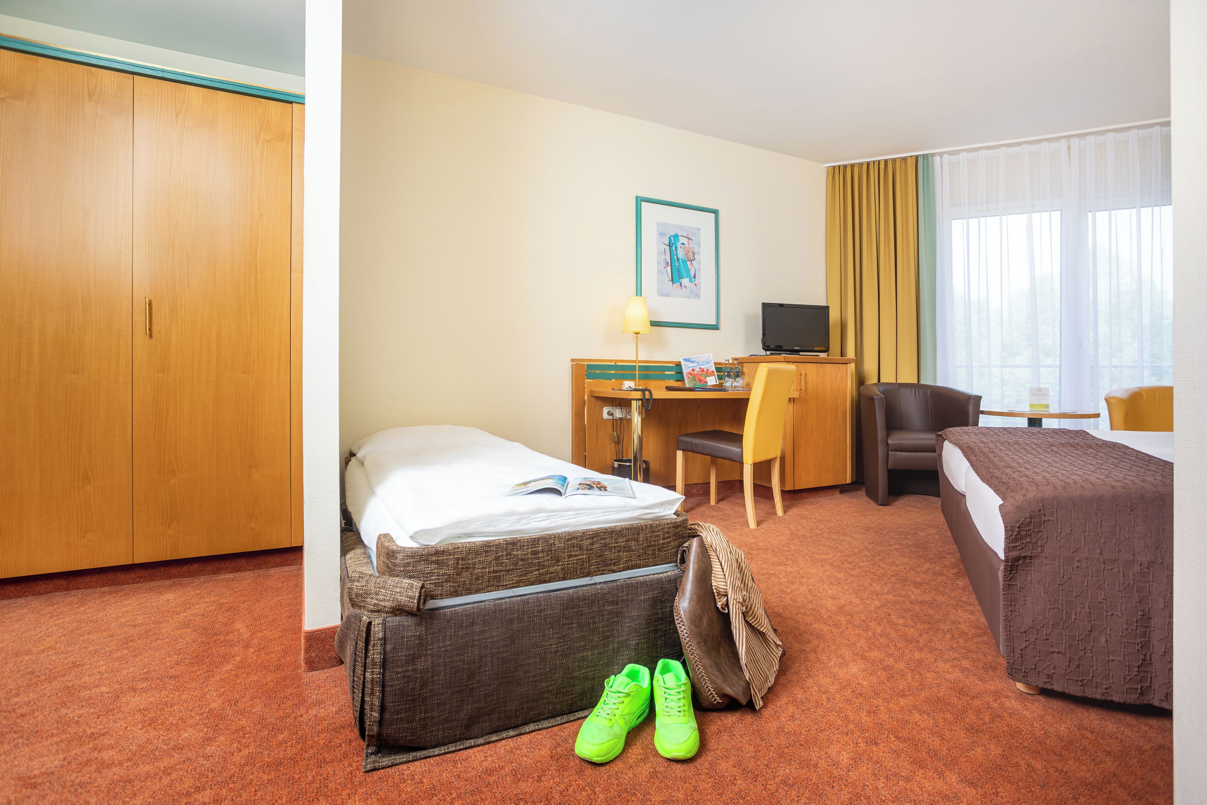 A hotel room with a bed, a desk with a computer, a chair, and a small table.