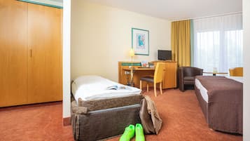 A hotel room with a bed, a desk with a computer, a chair, and a small table.