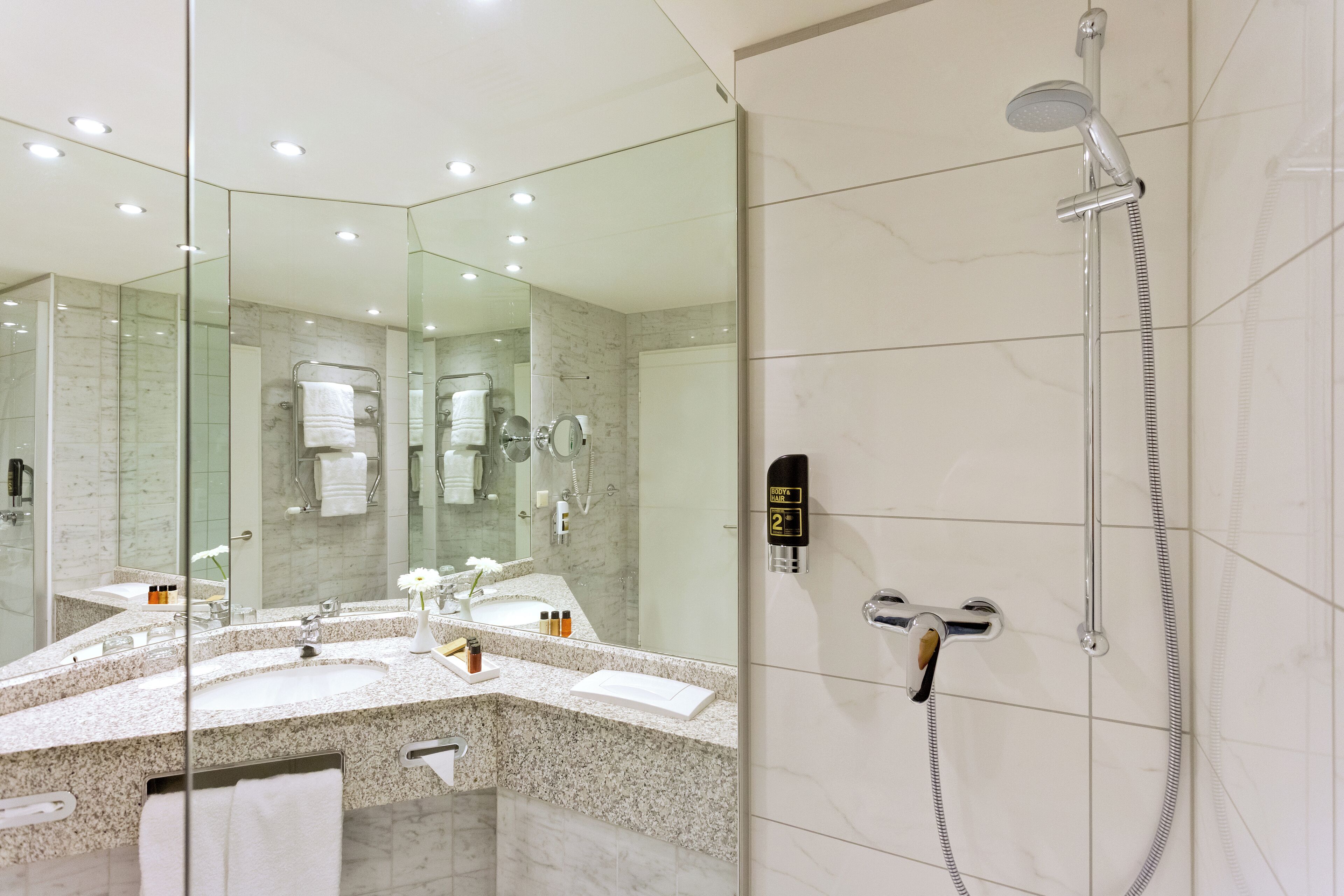 A modern bathroom with a large mirror, a shower, and a vanity with a sink and towel rack.