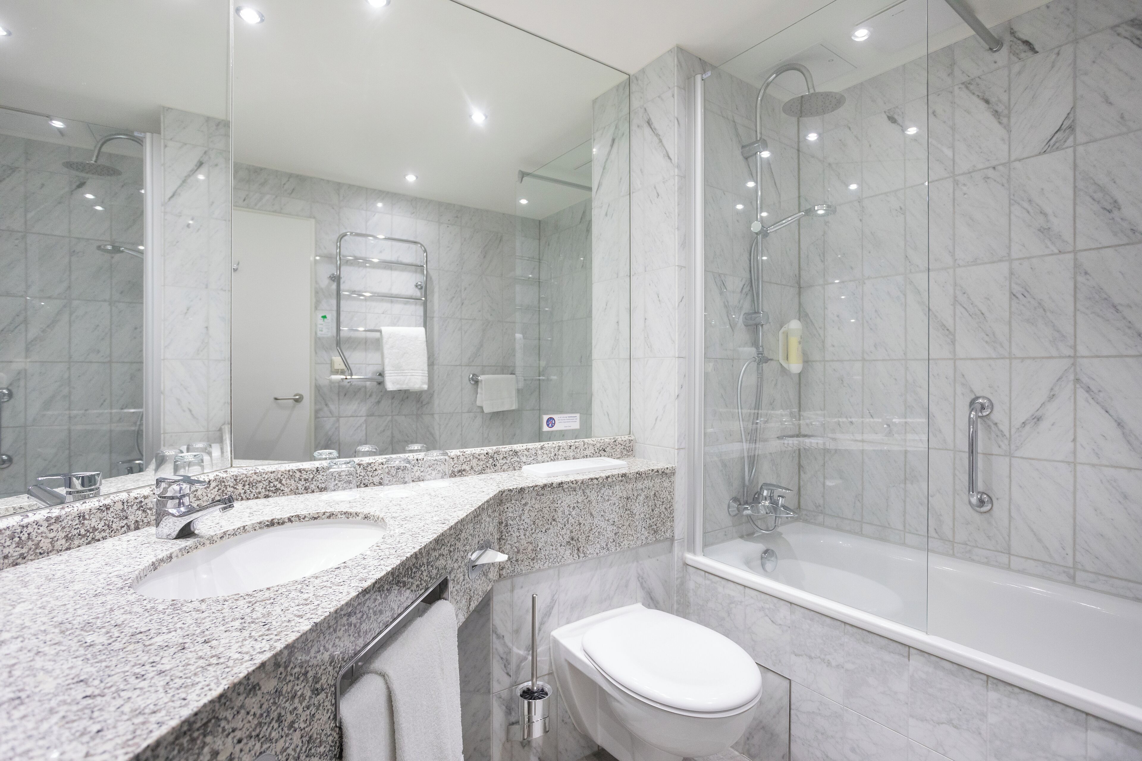 A modern bathroom with a large mirror, two sinks, a toilet, and a walk-in shower.