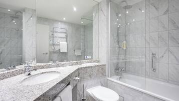 A modern bathroom with a large mirror, two sinks, a toilet, and a walk-in shower.