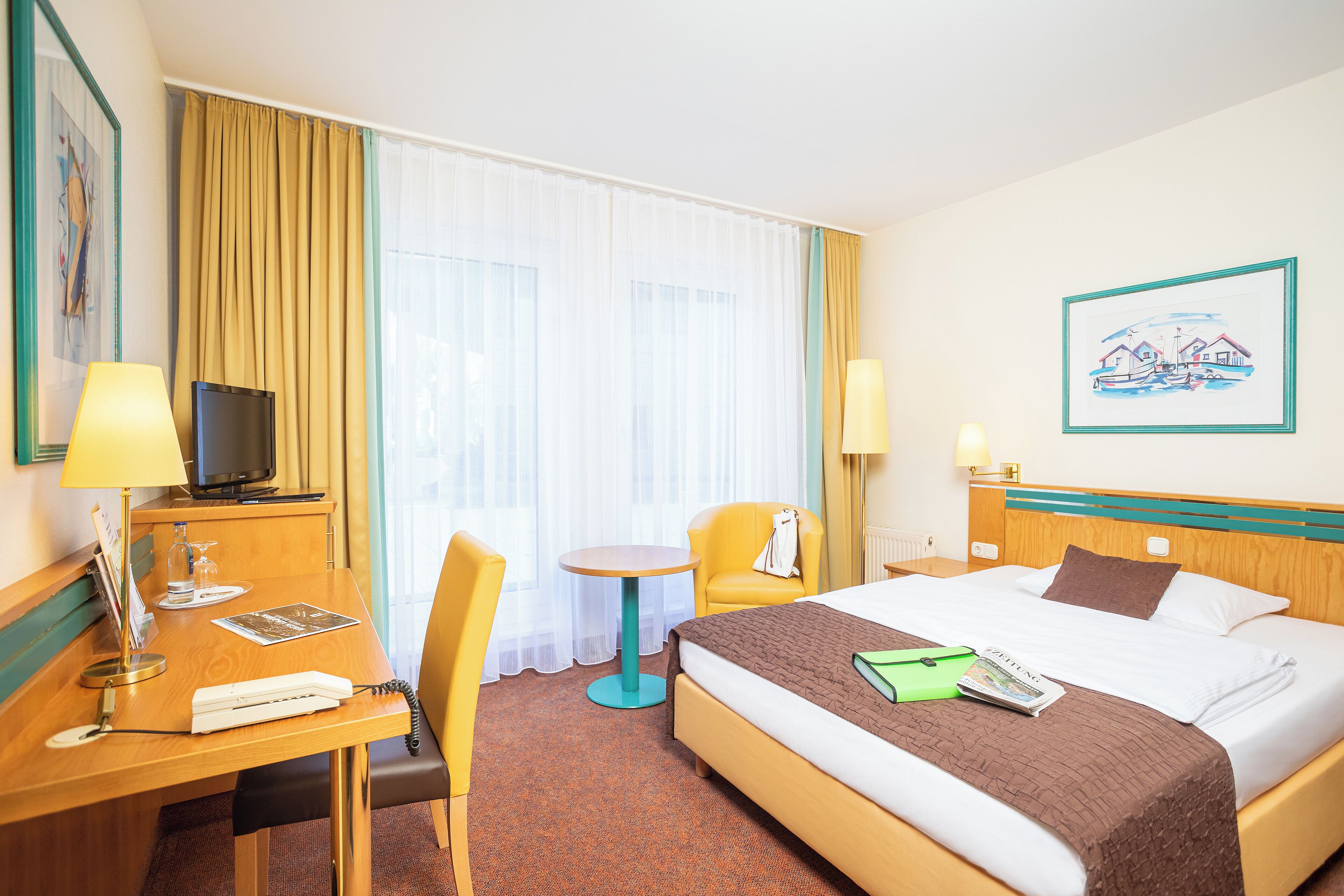 Une chambre d’hôtel comprenant un lit, un bureau avec une lampe, une chaise, une petite table et un téléviseur.