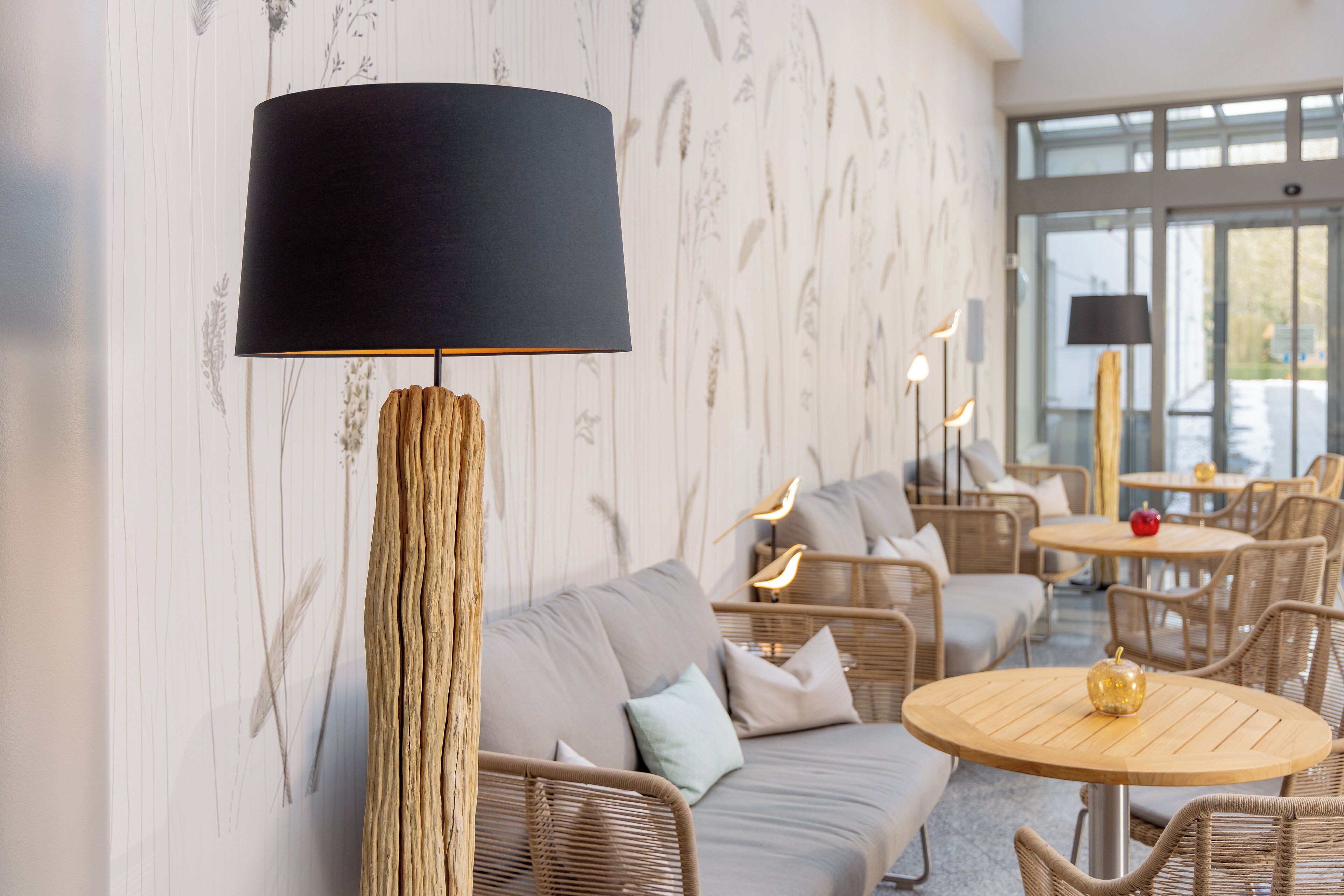 A modern interior with wicker furniture, a large black lamp, and a wall with a floral pattern.