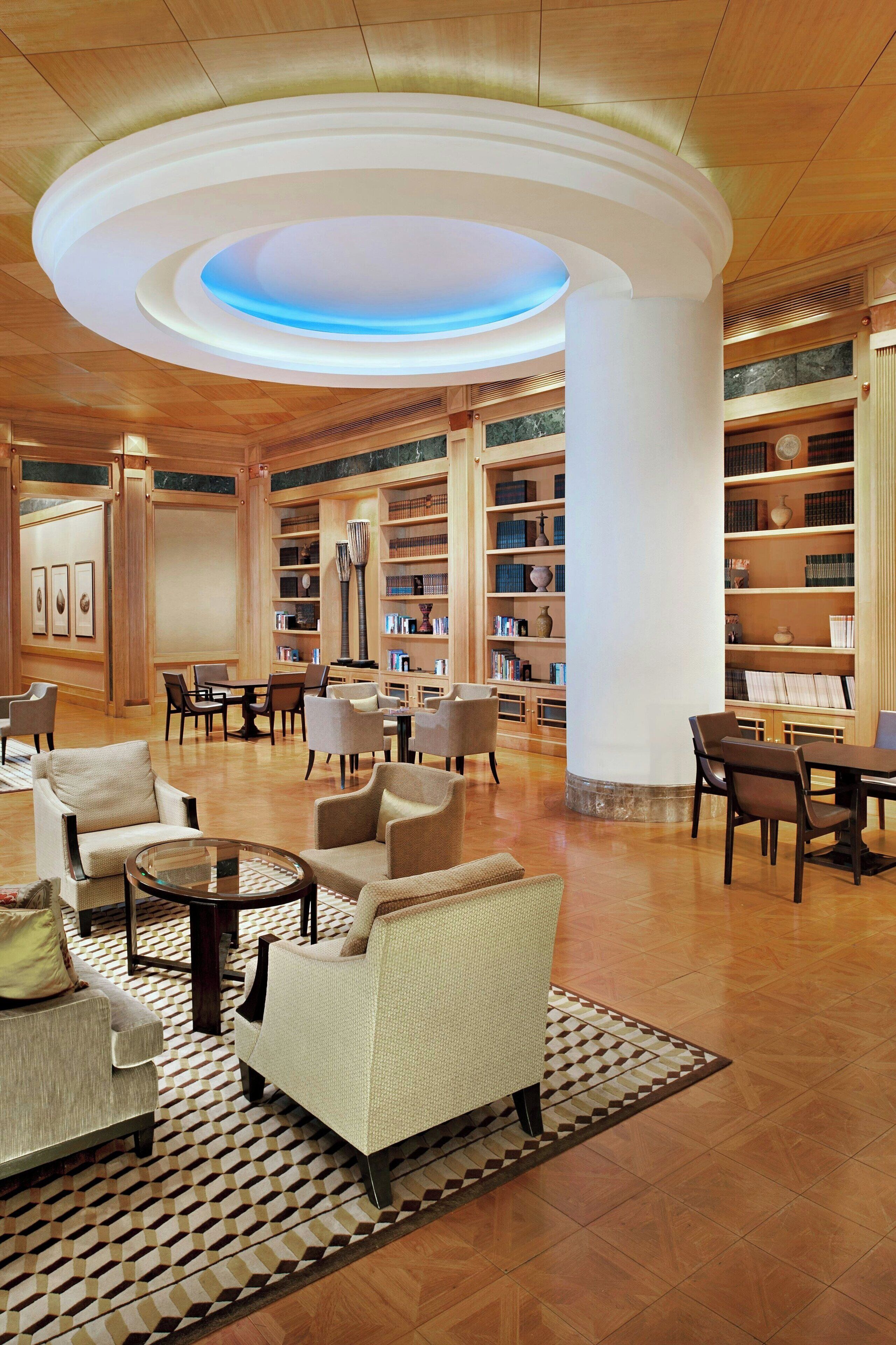 A spacious lobby with a central circular light fixture, multiple seating areas, and a large bookshelf filled with books and decorative items.