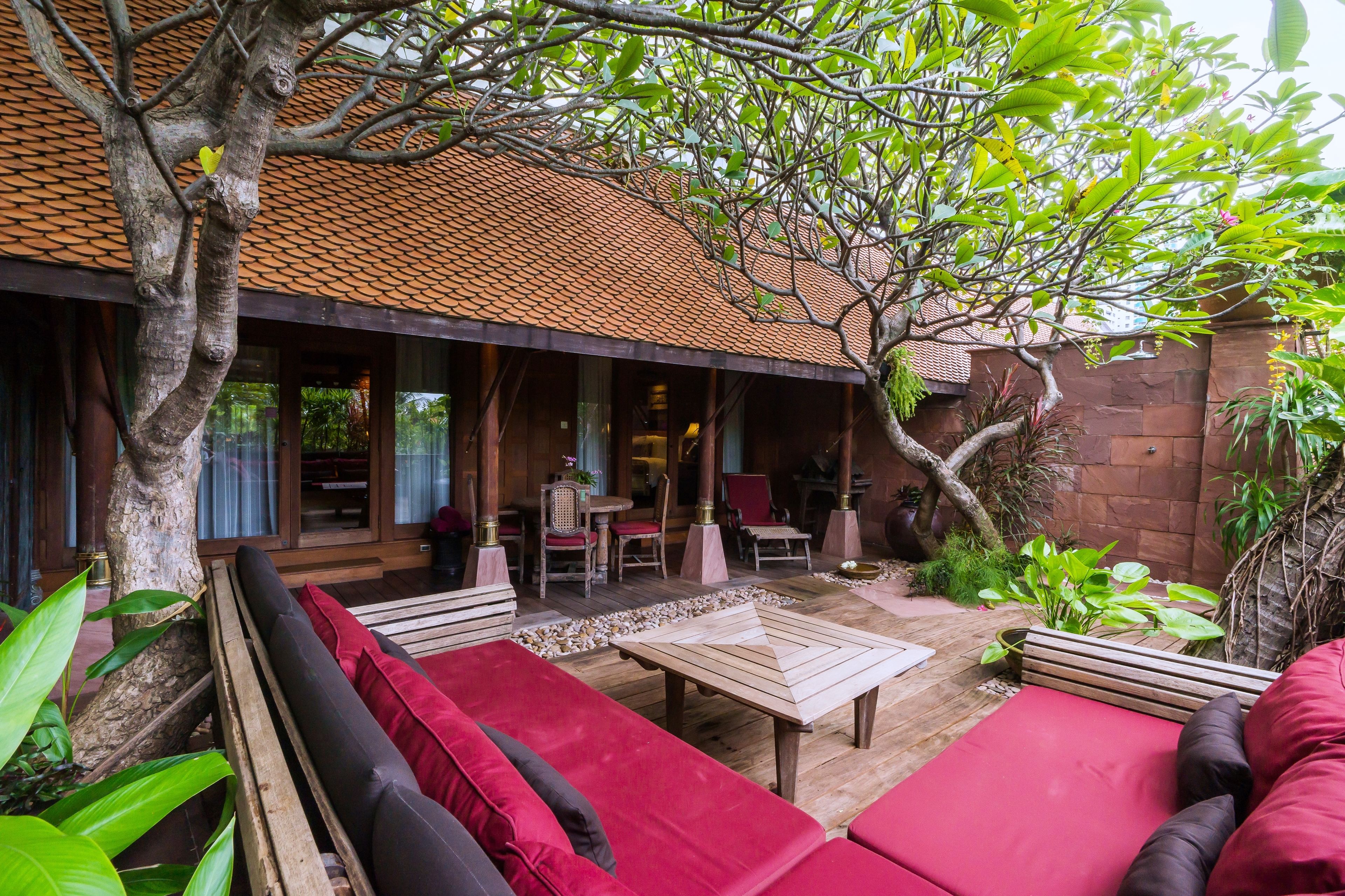 A covered outdoor seating area with red cushions, a wooden table, and chairs.