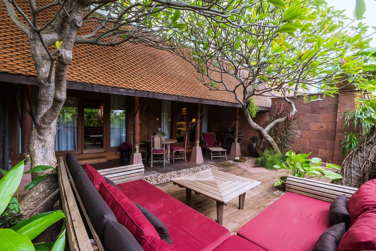 A covered outdoor seating area with red cushions, a wooden table, and chairs.