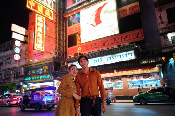Una pareja parada frente a un edificio iluminado con letreros de neón y un gran anuncio.