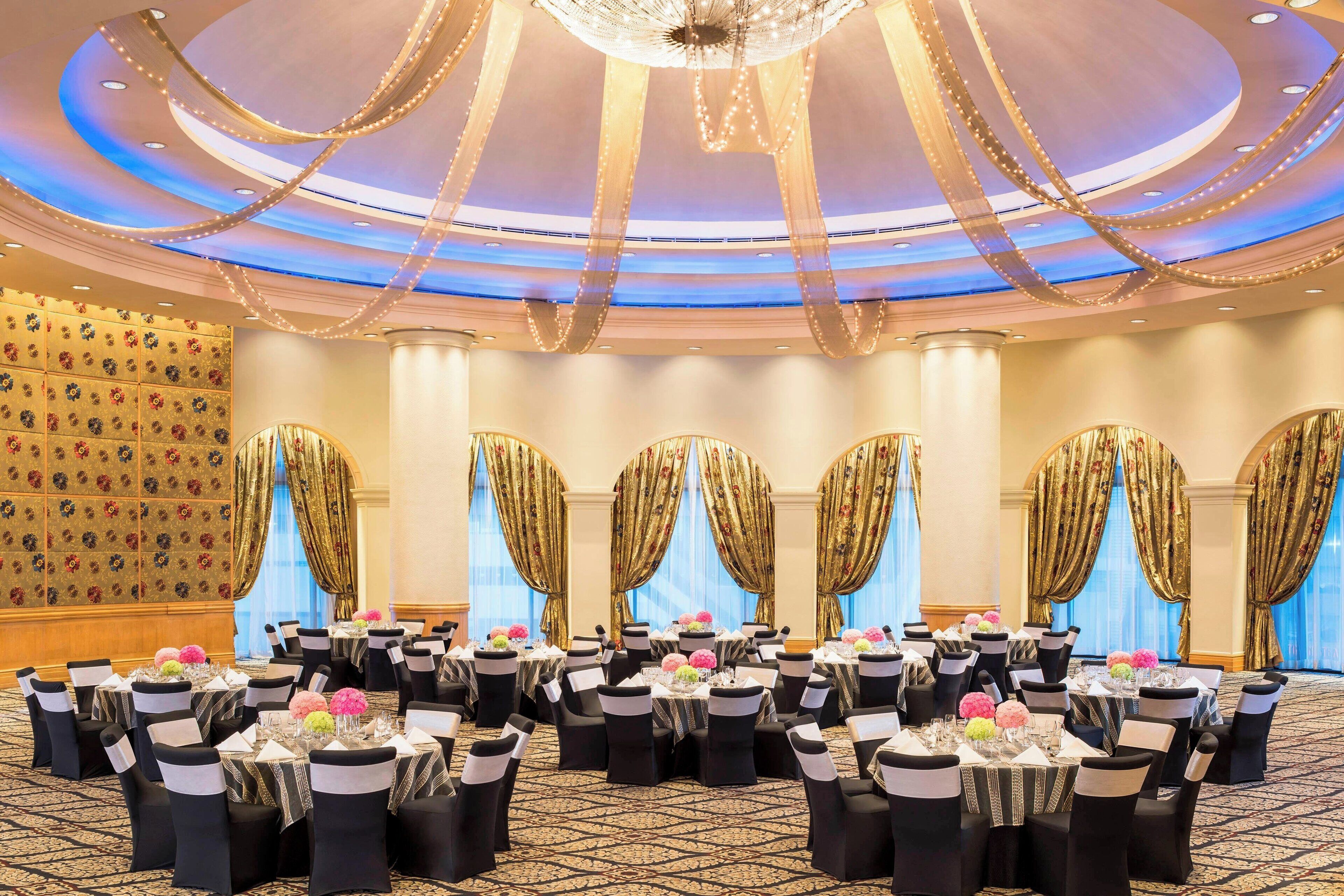Un salón de banquetes con mesas redondas, sillas negras y cortinas doradas.