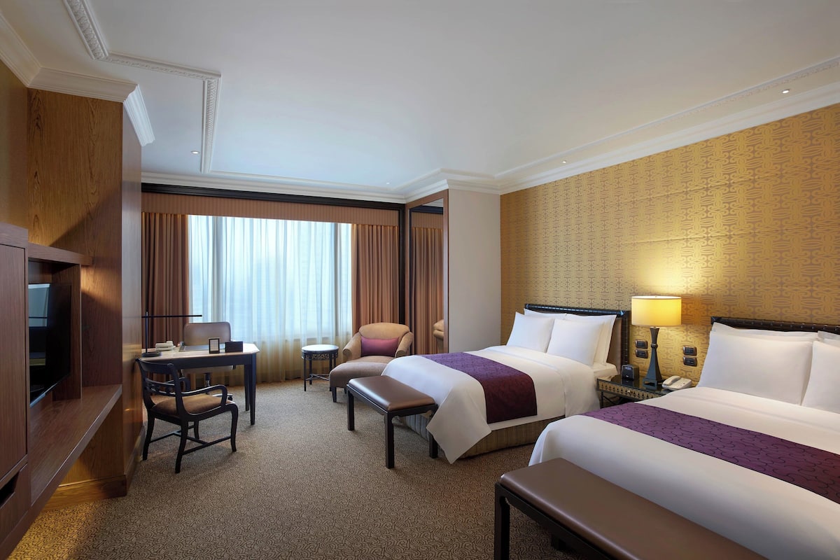 A hotel room with a large bed, a desk with a chair, a small table, and a TV.