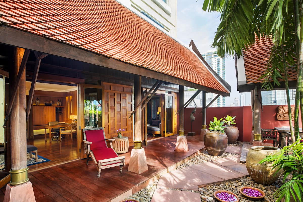A traditional wooden structure with a tiled roof, a red cushioned chair, and a dining area with a table and chairs.