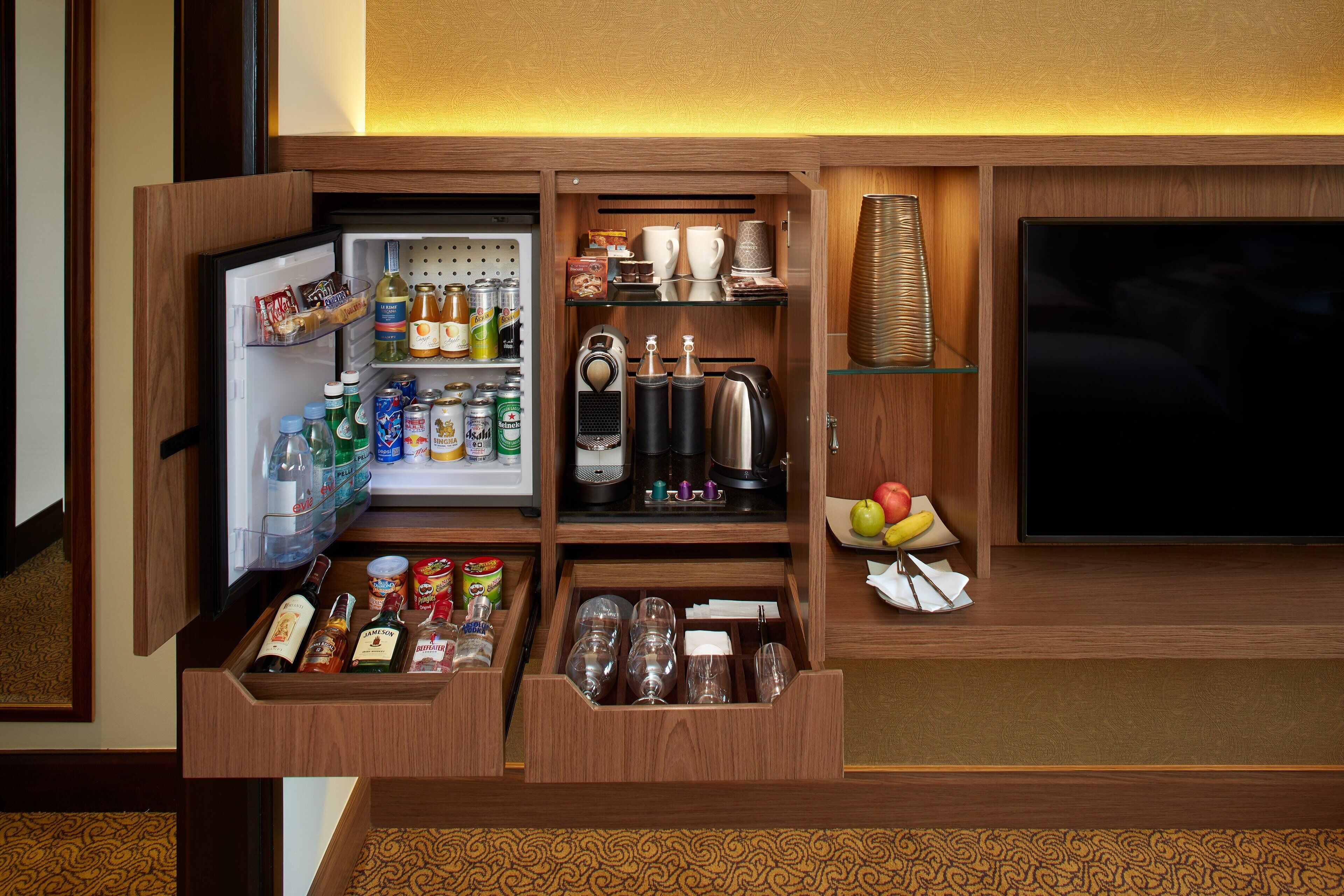 A compact minibar with a refrigerator, shelves with snacks, a coffee maker, and a TV.