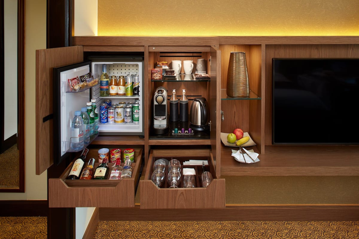 A compact minibar with a refrigerator, shelves with snacks, a coffee maker, and a TV.