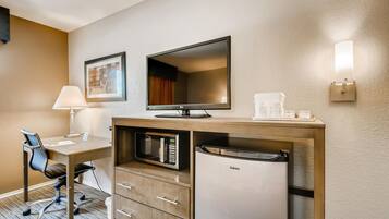 Une chambre d’hôtel équipée d’un bureau, d’une chaise, d’un four à micro-ondes, d’un réfrigérateur, d’une télévision à écran plat et d’une lampe fixée au mur.