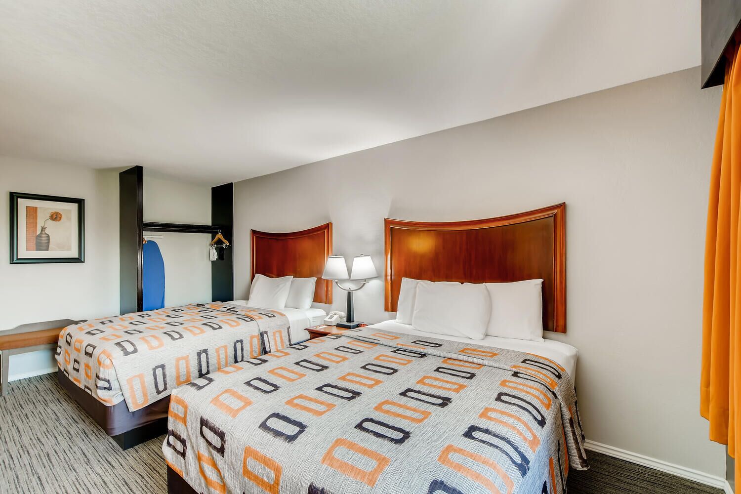 A hotel room with two beds, a desk, a chair, a lamp, and a framed picture on the wall.