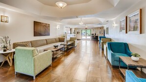 A spacious lobby with a high ceiling, a central seating area with sofas and chairs, a reception desk, and a view of the entrance.
