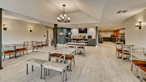 A spacious dining area with multiple tables and chairs, a central chandelier, and a kitchen in the background.