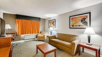A hotel room with a sofa, armchair, coffee table, TV, and lamp.