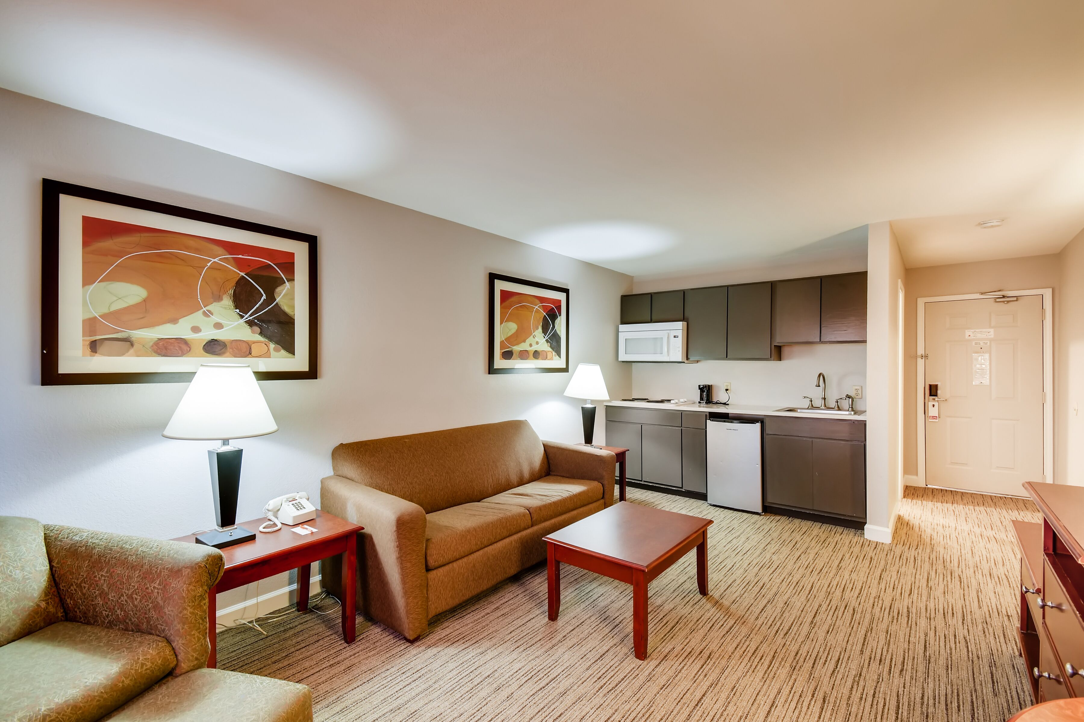 Habitación de hotel con sala de estar, sofá, mesa de centro, lámpara, teléfono, microondas y kitchenette.