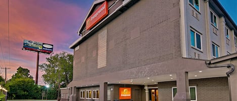 A hotel with a prominent orange sign, a brick facade, and a clear sky in the background.