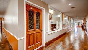 A long, well-lit hallway with a wooden door and white-framed windows.