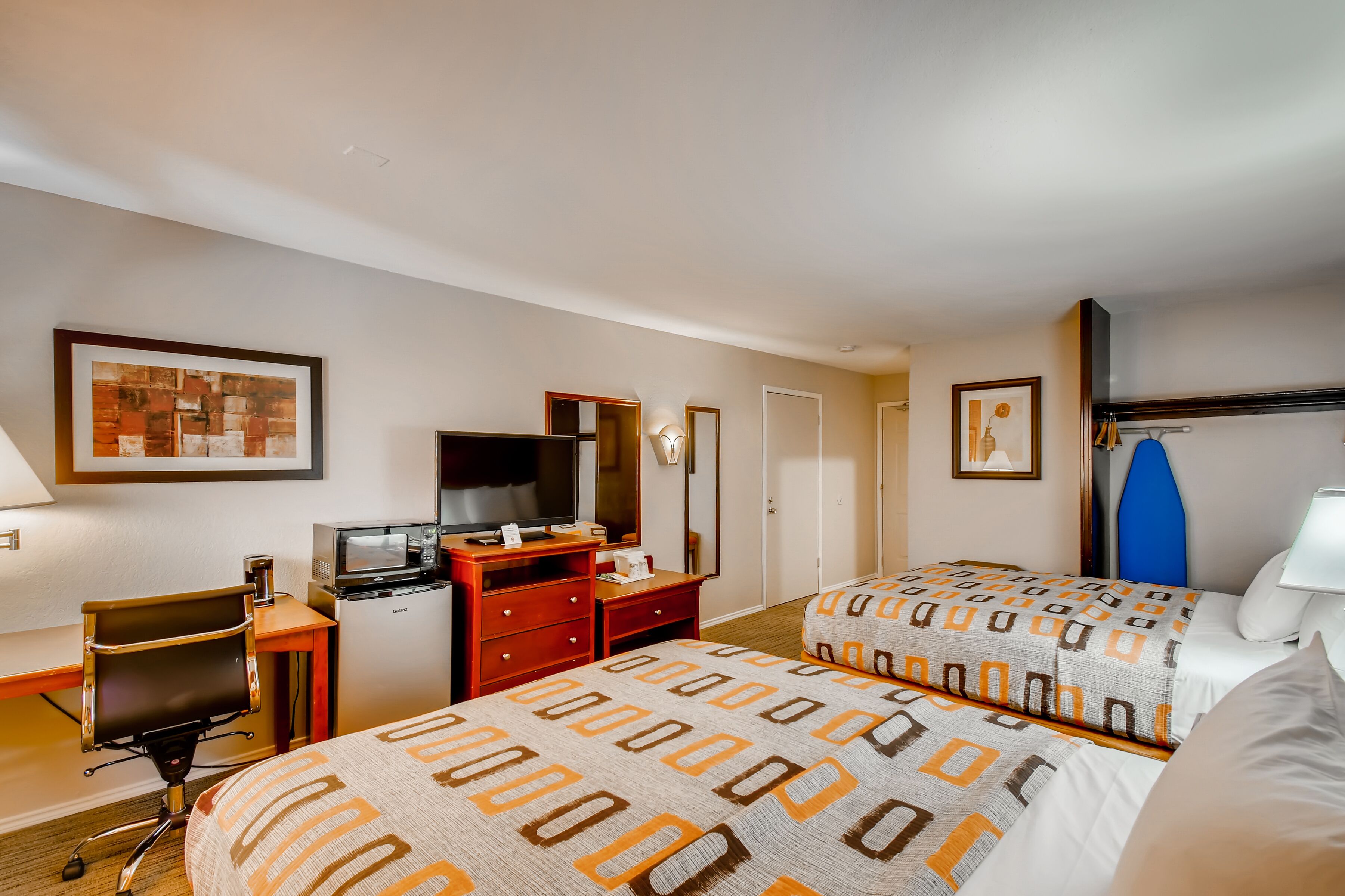 Une chambre d’hôtel avec deux lits, un bureau avec un ordinateur, une télévision et un petit réfrigérateur.