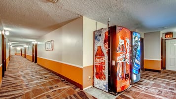 Pasillo de hotel con alfombra estampada, una máquina expendedora de Coca-Cola y señal de salida.
